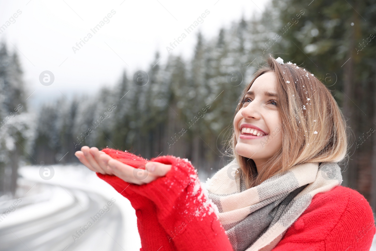 Photo of Young woman in warm clothes catching snow outdoors, space for text. Winter vacation