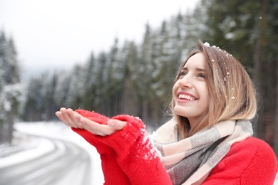 Photo of Young woman in warm clothes catching snow outdoors, space for text. Winter vacation