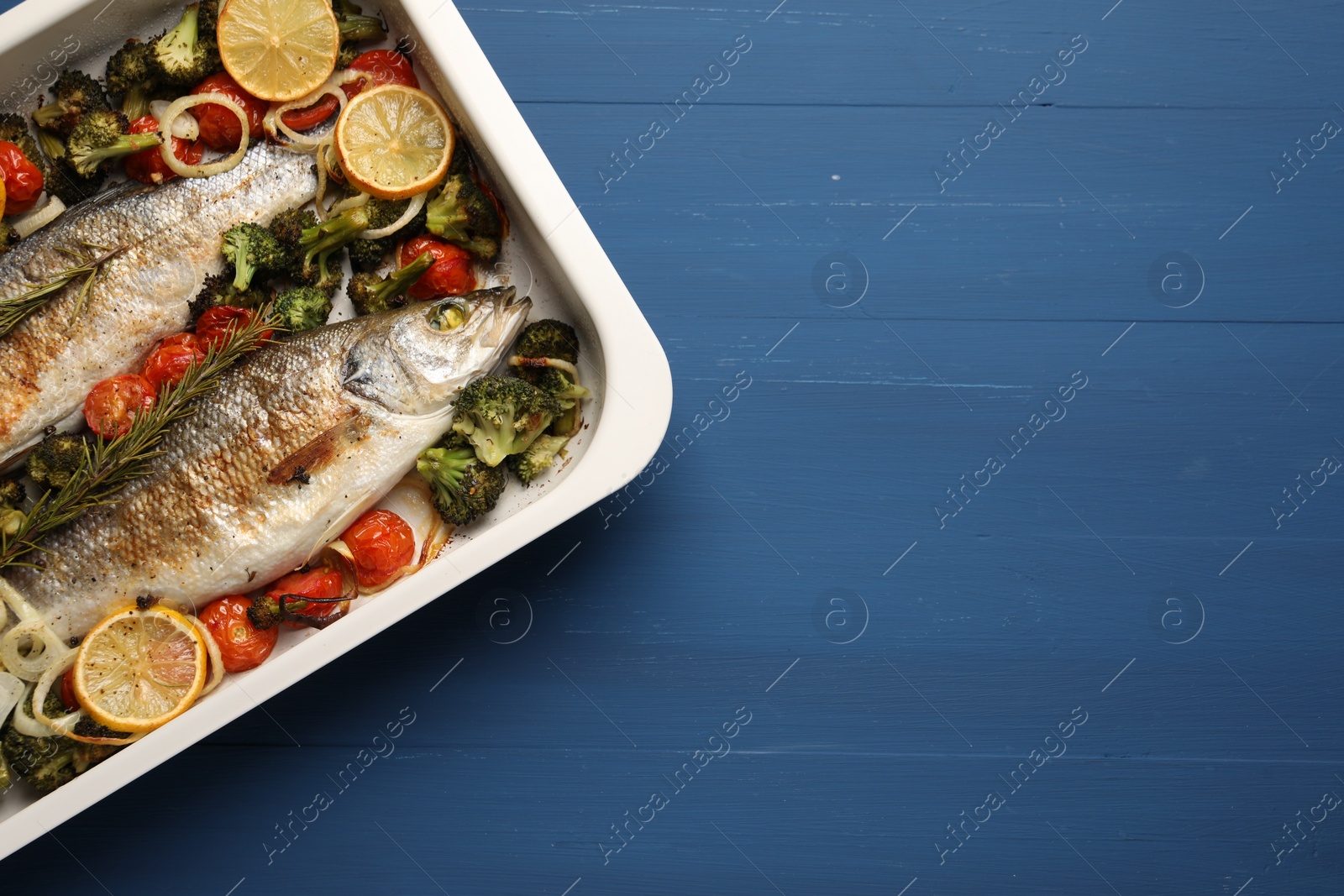 Photo of Delicious fish with vegetables and lemon in baking dish on blue wooden table, top view. Space for text