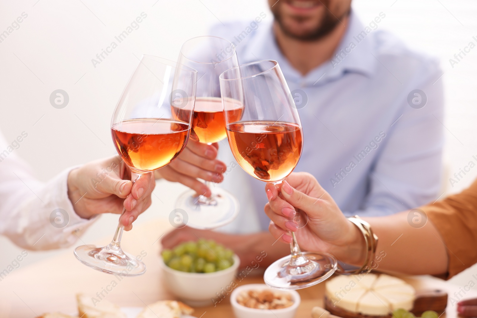 Photo of People clinking glasses with rose wine above table, closeup