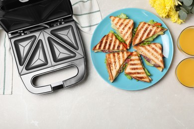 Modern grill maker and sandwiches on white table, flat lay. Space for text