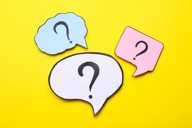 Different paper speech bubbles with question marks on yellow background, flat lay