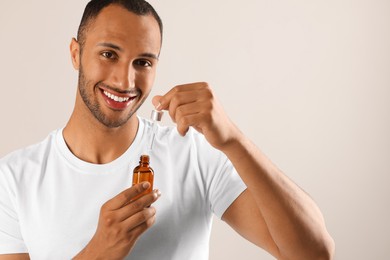 Handsome man with cosmetic serum in hands on light grey background, space for text