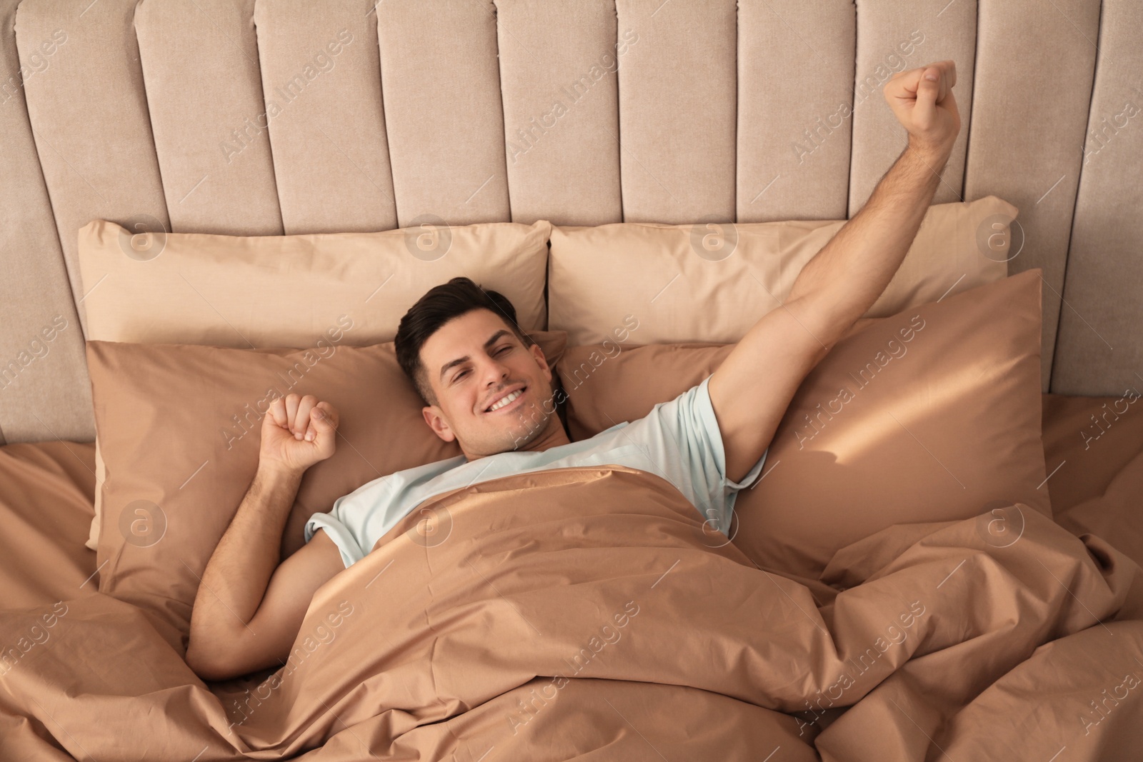 Photo of Man stretching in bed with brown linens at home, above view