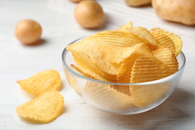 Photo of Bowl of crispy potato chips on white wooden table