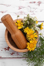 Photo of Mortar with pestle, flowers and herbs on white wooden table, flat lay