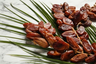 Tasty sweet dried dates and palm leaf on white marble table, closeup