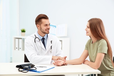 Doctor checking young woman's pulse in hospital