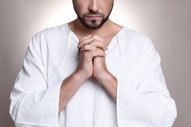 Photo of Religious man with clasped hands praying against grey background, closeup