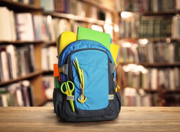 Backpack with school stationery on wooden table in library