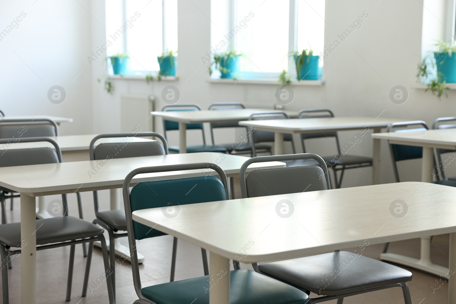 Photo of Empty school classroom with desks, windows and chairs