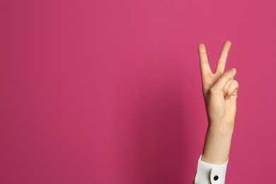 Photo of Young woman showing victory gesture on color background. Space for text
