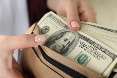 Photo of Money exchange. Woman putting dollar banknotes into wallet on blurred background, closeup