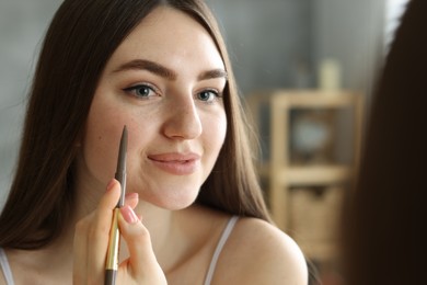 Photo of Beautiful woman drawing freckles with pen indoors