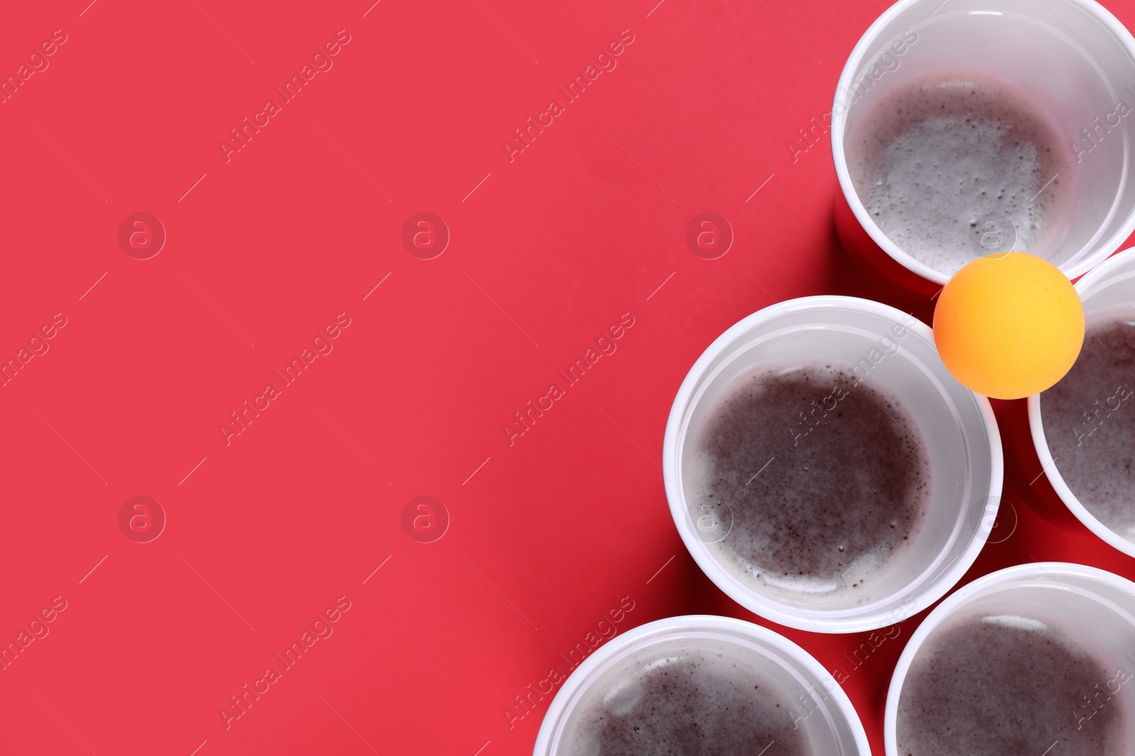 Photo of Plastic cups and ball on red background, flat lay with space for text. Beer pong game