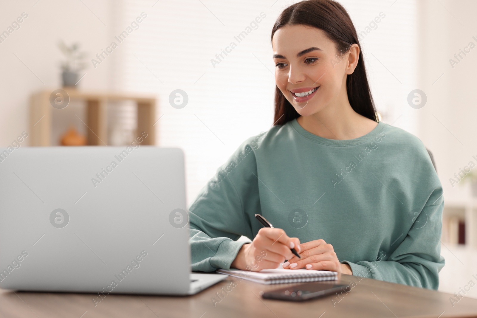 Photo of Young woman watching webinar at table in room