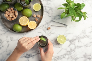 Young woman making delicious mint julep cocktail at table, top view