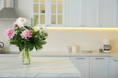 Photo of Peony bouquet on white marble table in kitchen interior