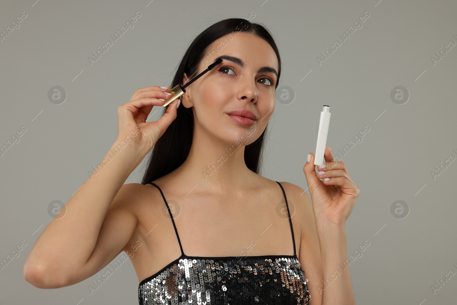 Photo of Beautiful young woman applying mascara on grey background