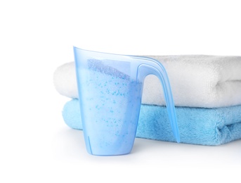 Laundry detergent in plastic measuring cup and towels on white background