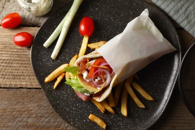 Delicious pita wrap with prosciutto, vegetables and potato fries on wooden table, top view