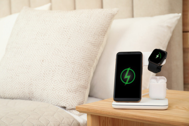 Photo of Different gadgets charging on wireless pad in bedroom. Space for text