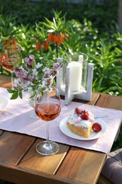 Photo of Vase with spring flowers, wine and cake on table served for romantic date in garden