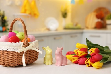 Photo of Easter decorations. Wicker basket with painted eggs, tulips and bunny figures on white table indoors, closeup