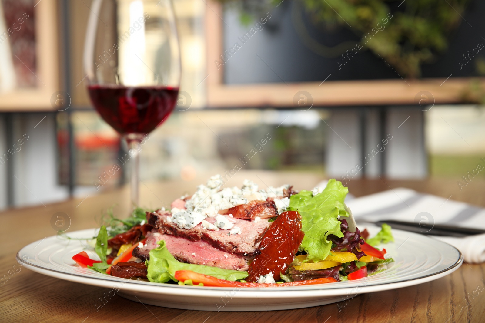 Photo of Delicious salad with roasted meat and vegetables served on wooden table indoors. Space for text