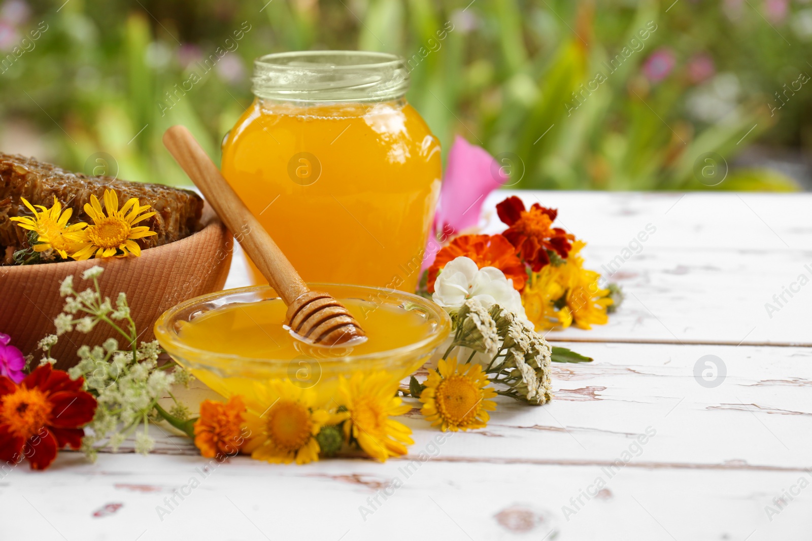 Photo of Delicious honey, combs and different flowers on white wooden table in garden. Space for text