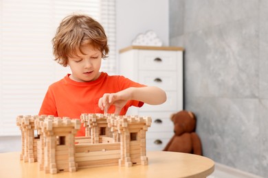 Cute little boy playing with wooden fortress at table in room. Child's toy