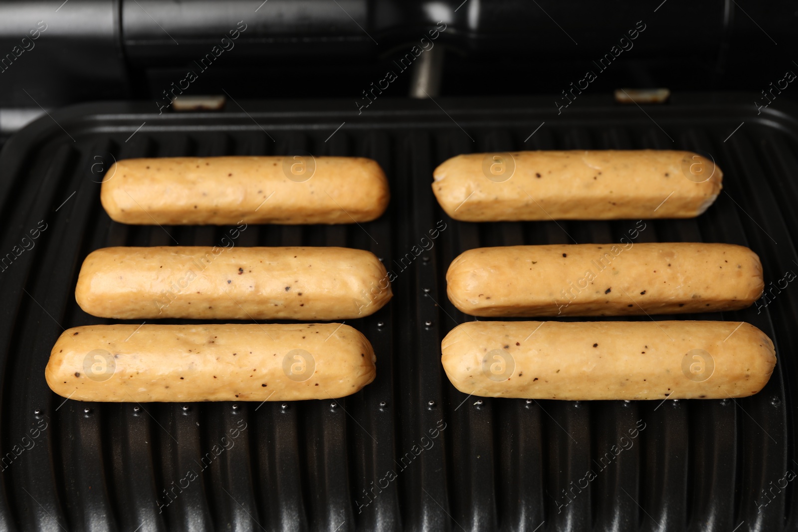 Photo of Delicious vegan sausages cooking on electric grill, closeup