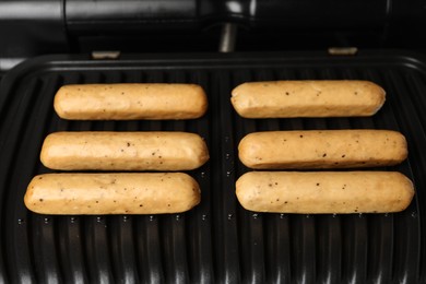 Photo of Delicious vegan sausages cooking on electric grill, closeup