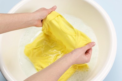 Photo of Woman washing baby clothes in basin on light blue background, closeup