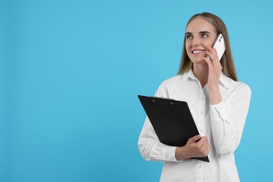 Photo of Happy young secretary with clipboard talking on smartphone against light blue background, space for text