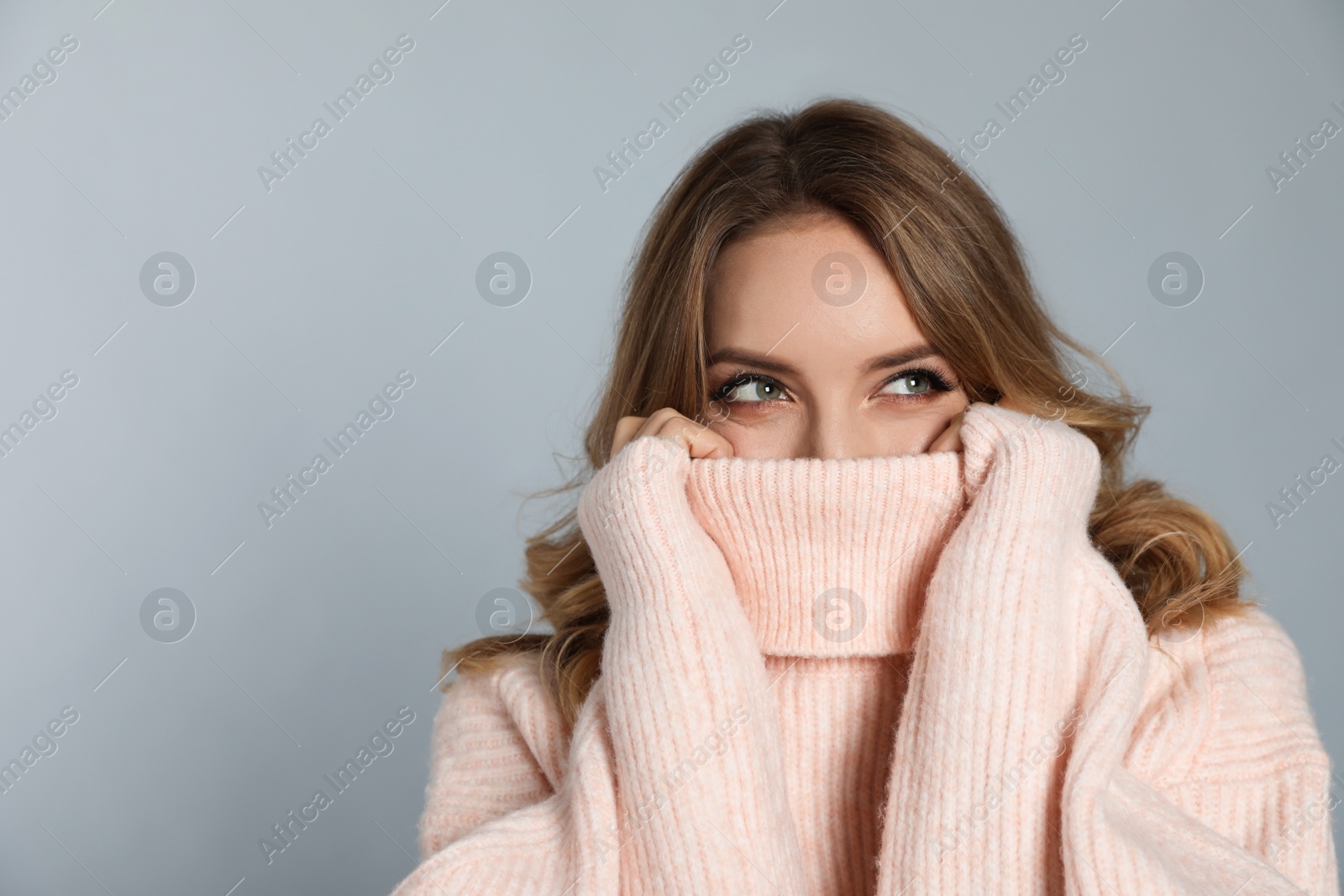 Photo of Happy young woman wearing warm sweater on grey background, space for text. Christmas celebration