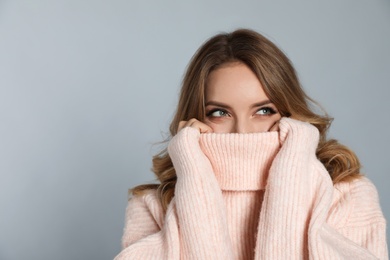 Happy young woman wearing warm sweater on grey background, space for text. Christmas celebration