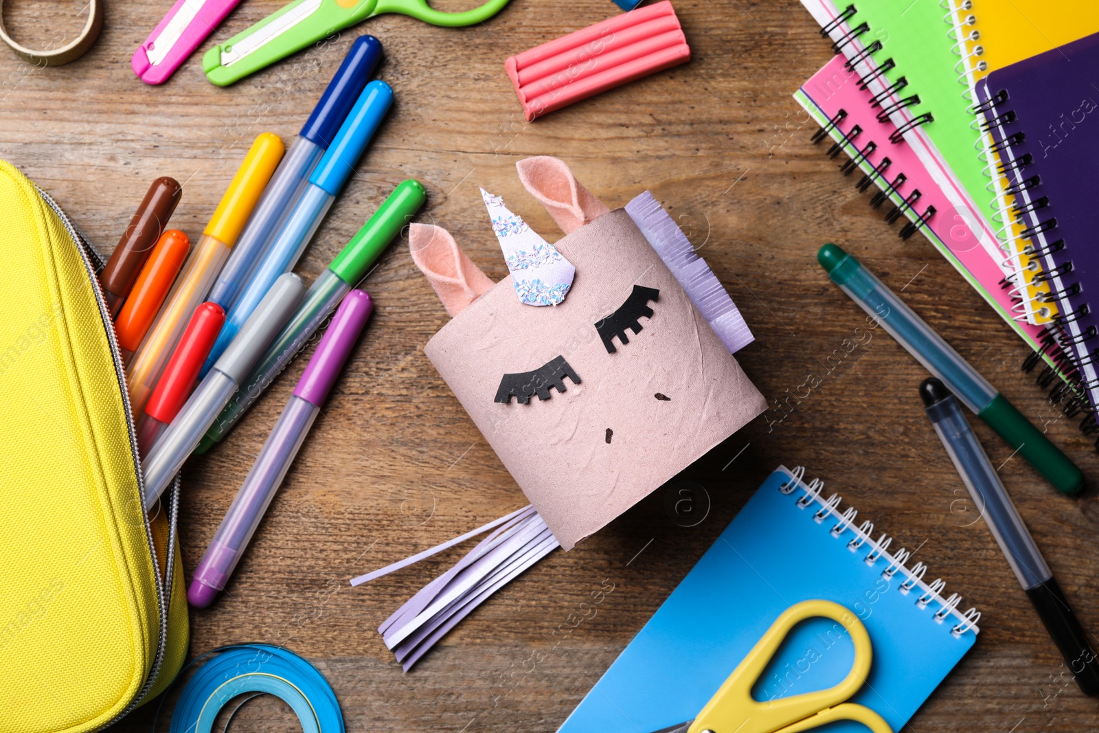Photo of Toy unicorn made of toilet paper roll among stationery  on wooden table, flat lay