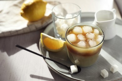 Photo of Refreshing iced coffee with milk in glass, sugar cubes and spoon on white wooden table, closeup