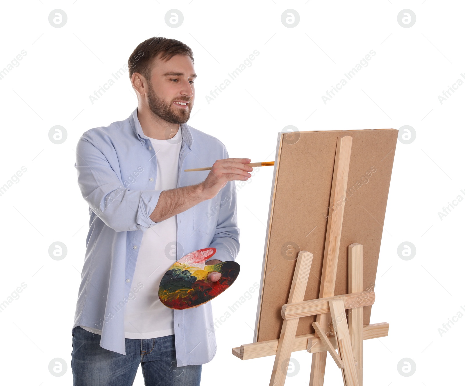 Photo of Man painting with brush on easel against white background. Young artist