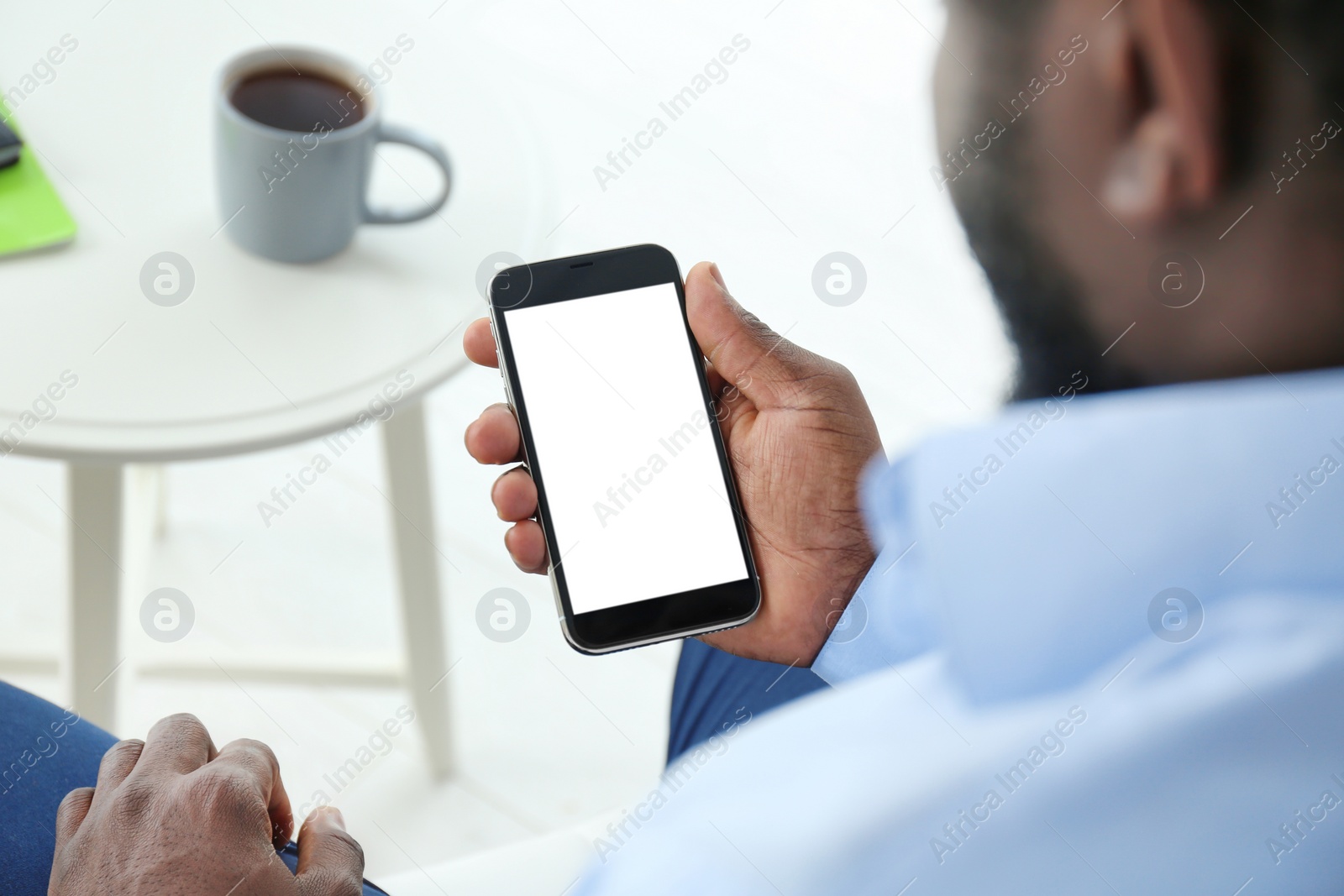 Photo of African-American man holding mobile phone with blank screen in hand indoors