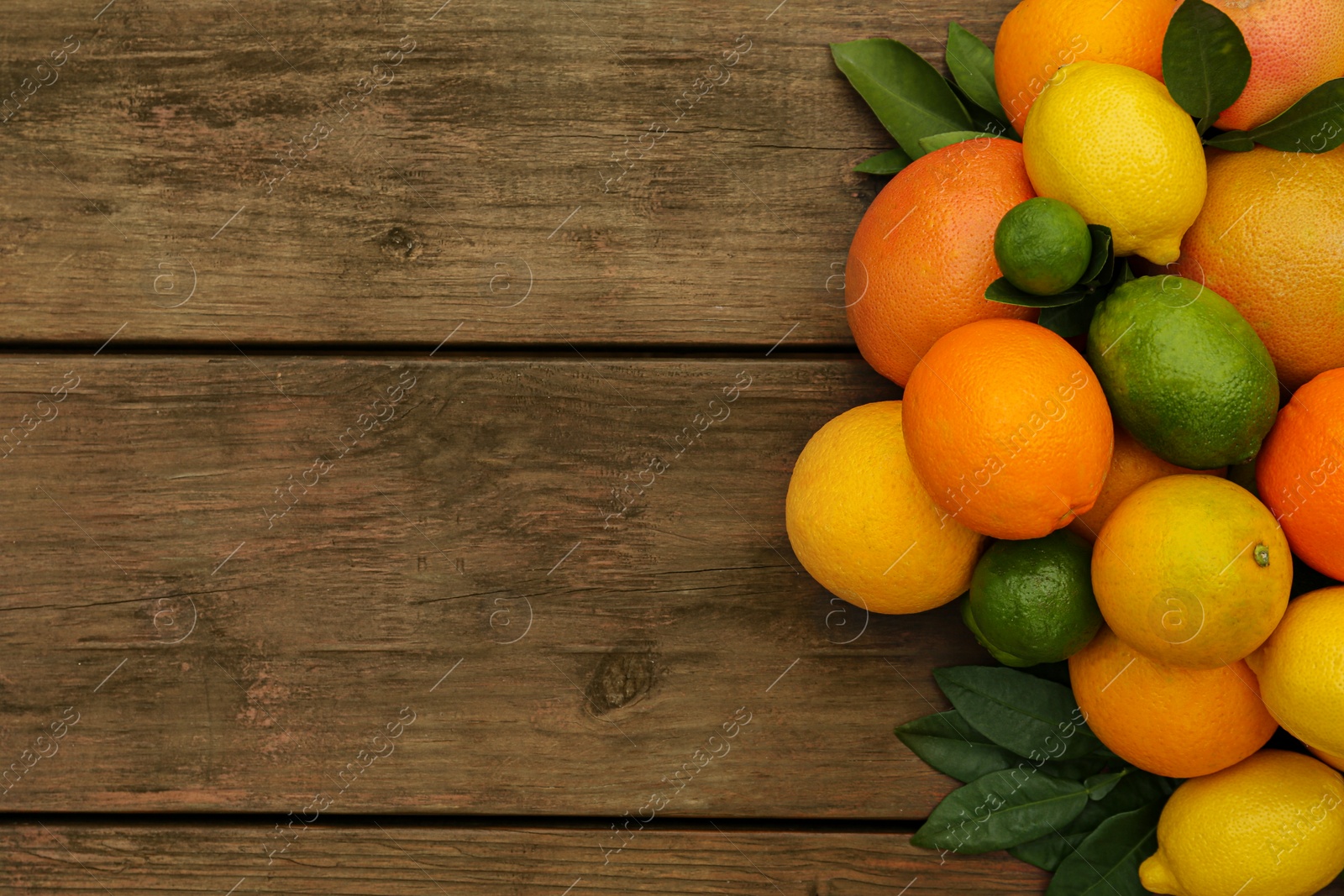 Photo of Different citrus fruits with green leaves on wooden table, flat lay. Space for text