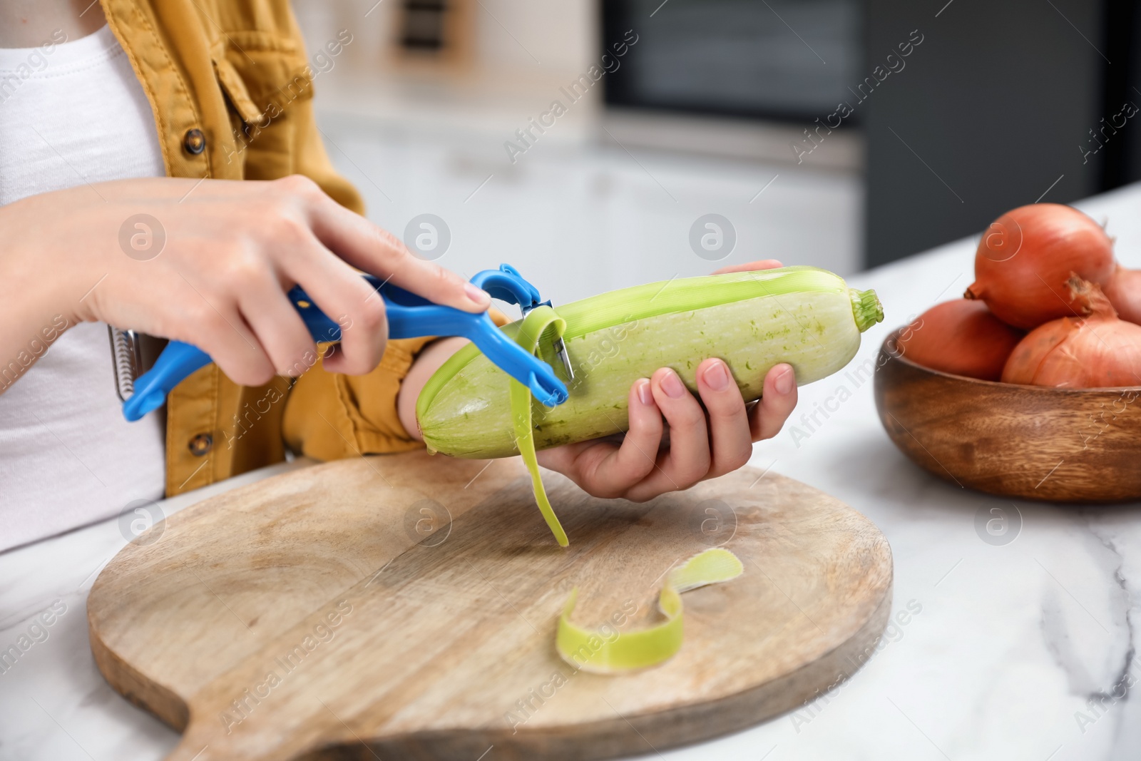 Photo of Woman peeling zucchini at table in kitchen, closeup. Preparing vegetable