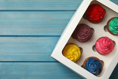 Box with different cupcakes on light blue wooden table, top view. Space for text