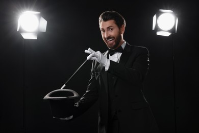 Happy magician showing magic trick with top hat on stage