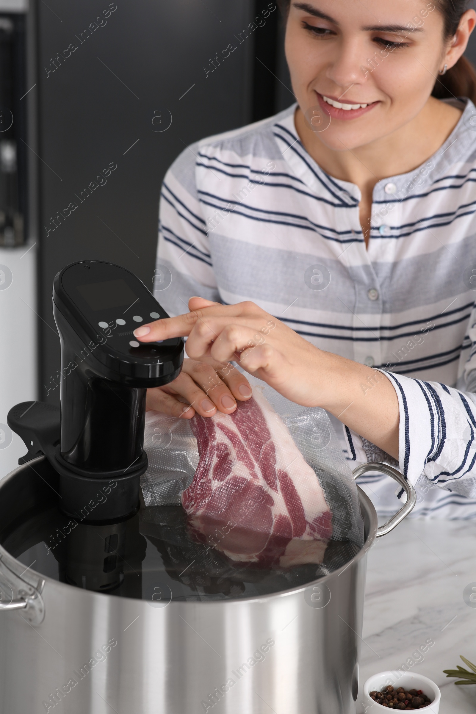 Photo of Woman putting vacuum packed meat into pot and using thermal immersion circulator. Sous vide cooking