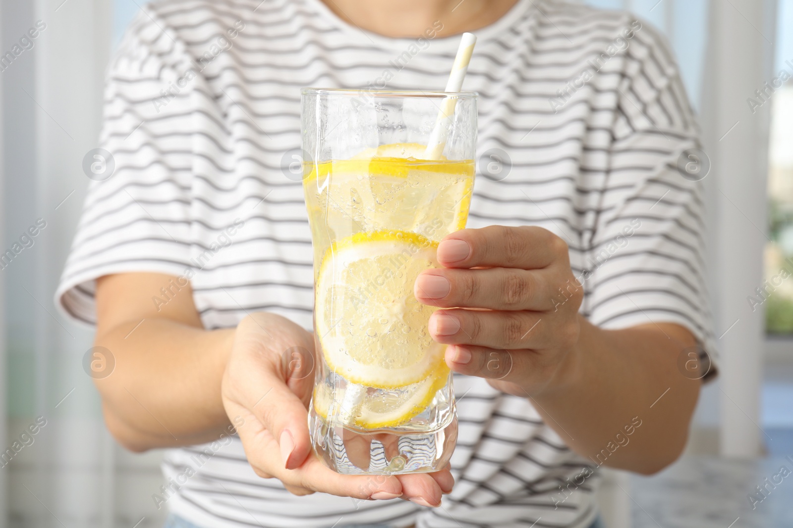 Photo of Woman holding glass of soda water with lemon slices indoors, closeup