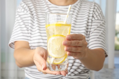 Photo of Woman holding glass of soda water with lemon slices indoors, closeup
