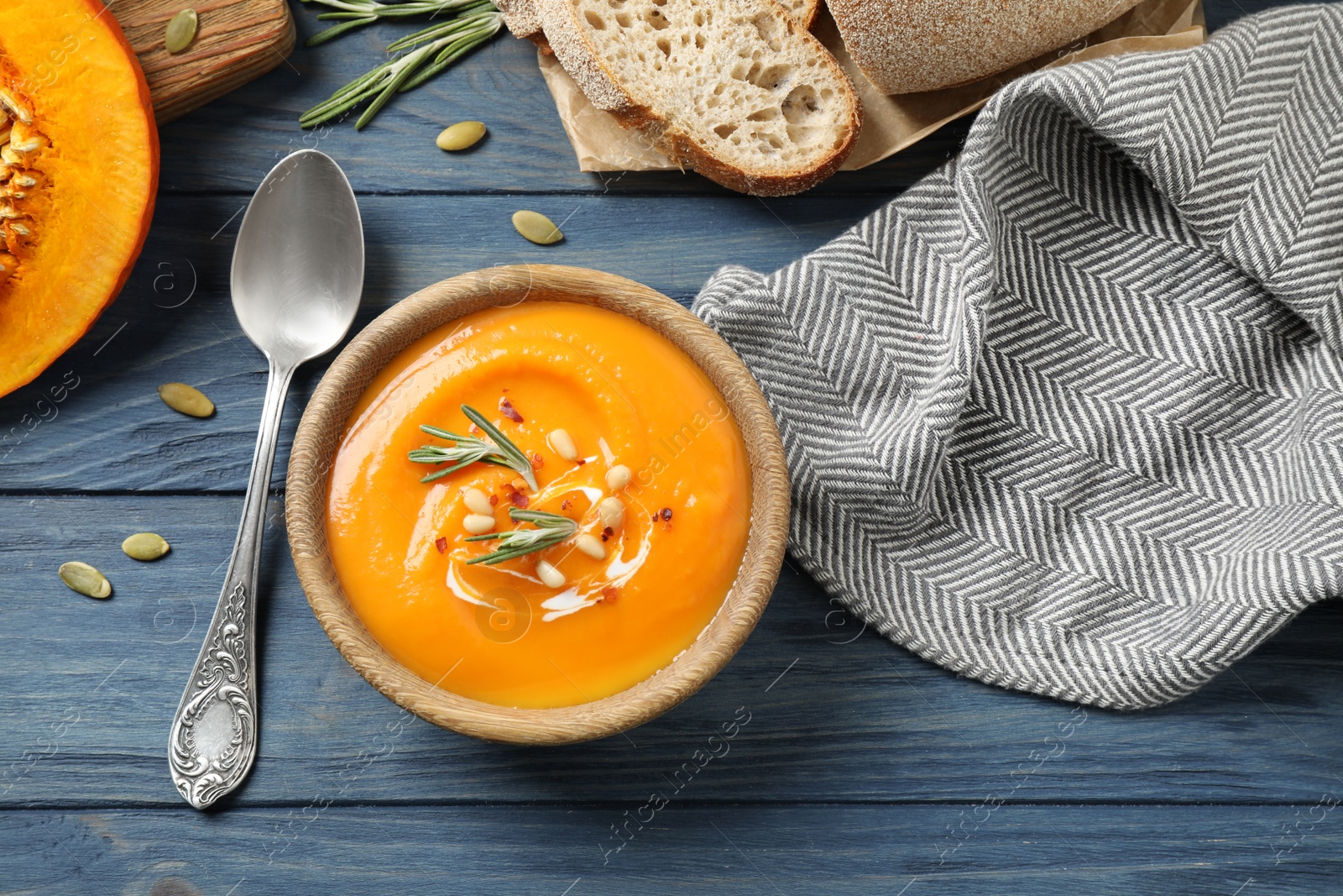 Photo of Delicious pumpkin soup in bowl on blue wooden table, flat lay