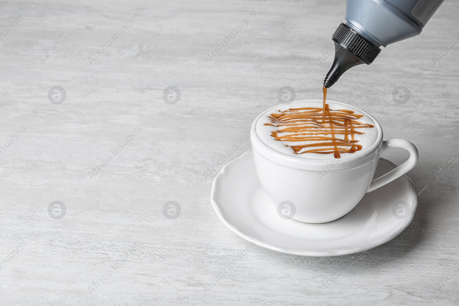 Photo of Adding caramel topping to latte macchiato on table, space for text